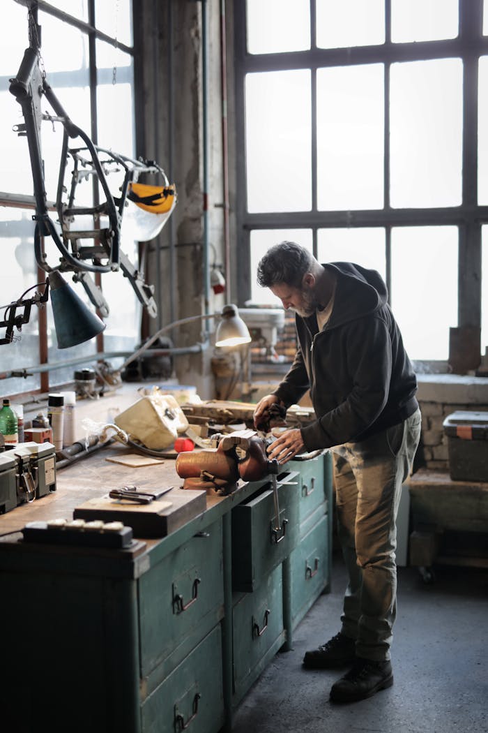 Side view of bearded male master in casual clothes standing at workbench and fixing details with professional metal instrument